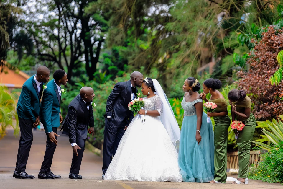 Wedding party laughing as the bride and groom share a kiss
